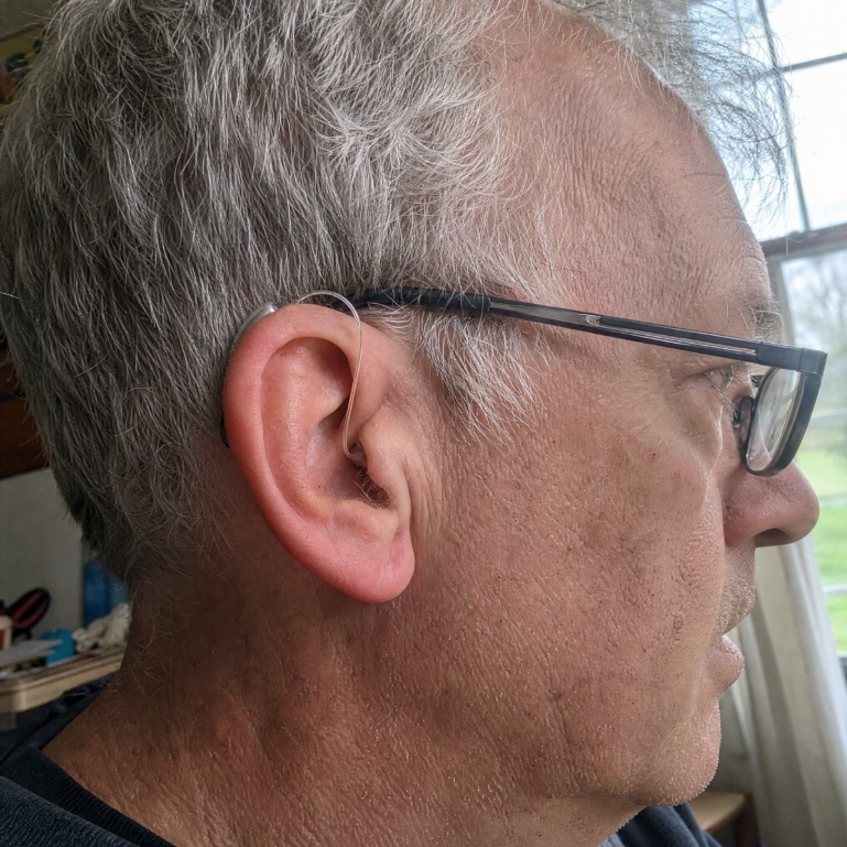 certus-max-discreet-behind-the-ear.jpgSide profile of a grey-haired man wearing glasses with a small silver Certus Max device behind his ear and a thin clear wire running into the ear canal.